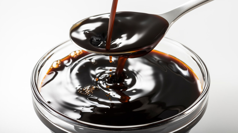 Dark brown Worscestershire sauce pouring into a spoon and bowl.
