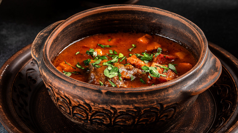 Ancient-looking soup with broth, meat, and greens in wooden or pottery bowl