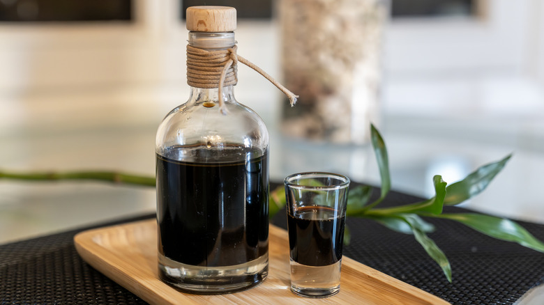 Coffee liqueur in bottle and glass on wooden board atop dark surface with decorations in background
