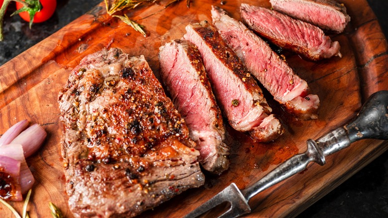 A ribeye steak cooked to medium doneness, sliced and served on a wooden board.
