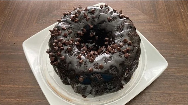 Chocolate bundt cake with chocolate glaze and chocolate chips on white plate.