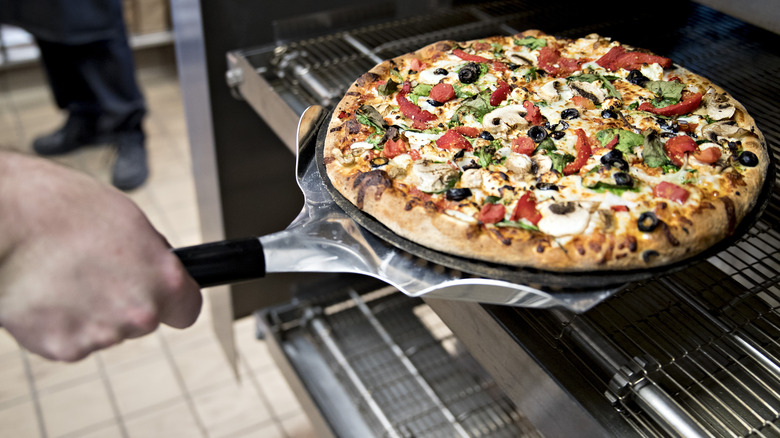 Domino's employee placing sausage pizza in oven