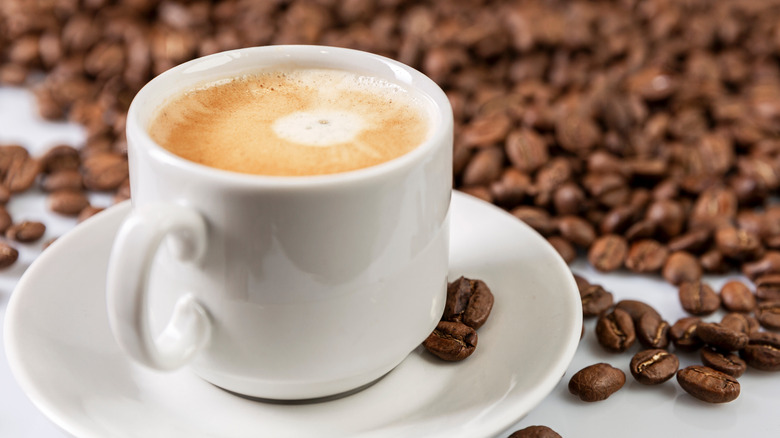 Cup of coffee sitting next to pile of coffee beans