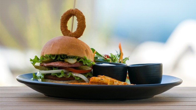 A gourmet hamburger served on a cruise, with two deck chairs in the background.