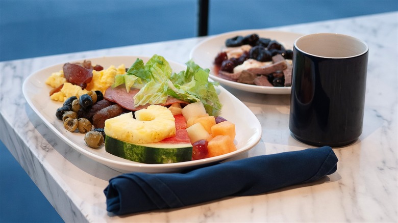 Fruits, greens, meats, and desserts from a cruise ship buffet, along with a beverage in a black cup.