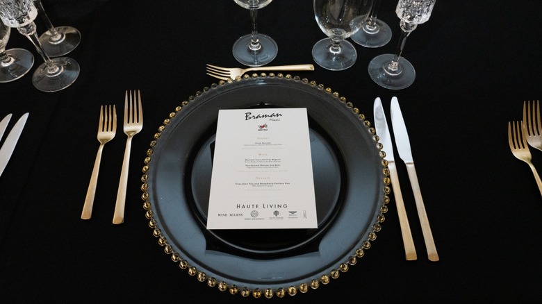 Fancy table setting on black tablecloth with gold utensils