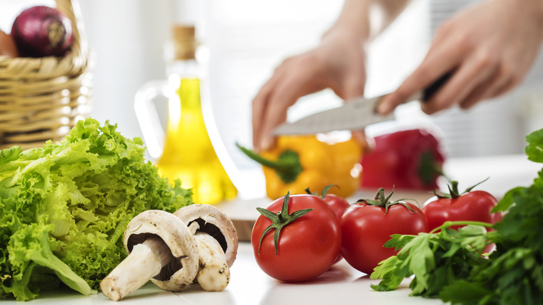 Person cutting vegetables with olive oil in background