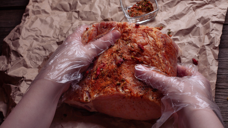 Hands applying dry rub to raw meat