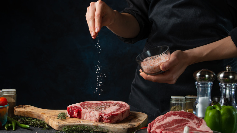 Chef hands sprinkle salt on raw steak