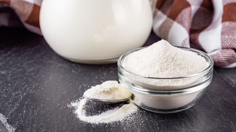 A bowl of milk powder next to a jug of milk