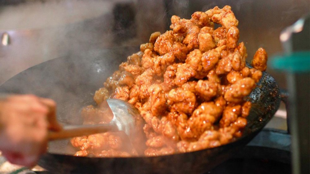 Orange chicken being tossed in a wok over stovetop.