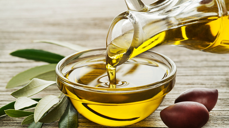 olive oil pouring from glass bottle into bowl