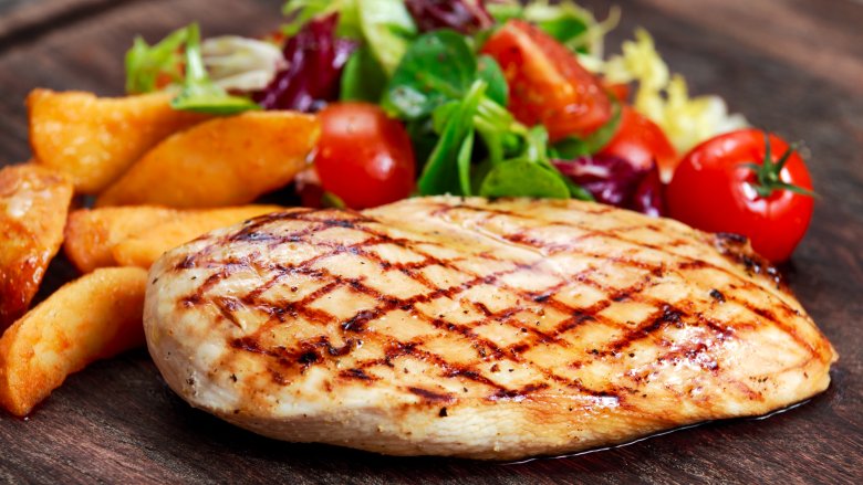 chicken breast on a serving platter with potato wedges and tomatoes