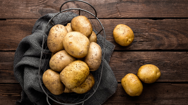 Yellow potatoes piled in a metal basket on a gray cloth on a dark brown wooden surface