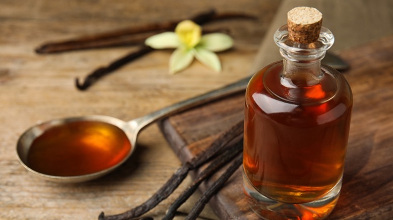 Bottle of vanilla extract alongside vanilla bean pods and tablespoon of vanilla extract