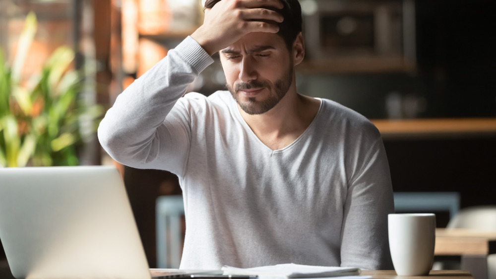 Man with headache, computer, and cup of coffee