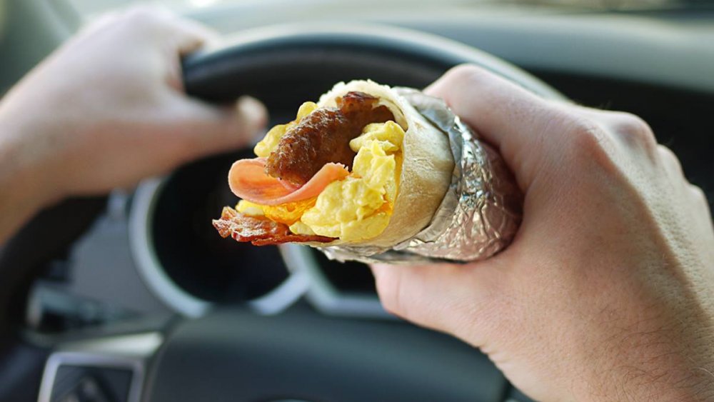 Jack in the Box breakfast burrito in the hand of a man driving a car