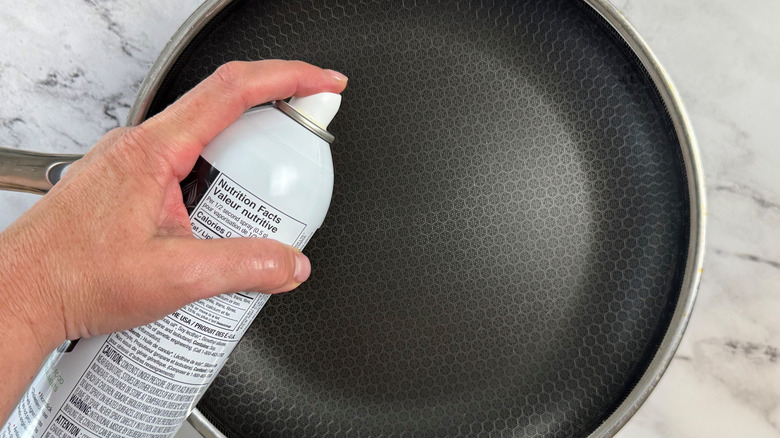 Hand holding bottle of cooking spray over pan