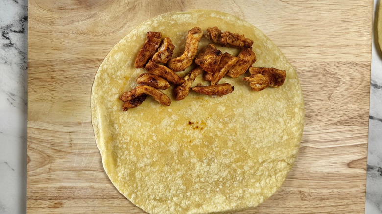Tortilla on wooden board partially covered with pieces of chicken