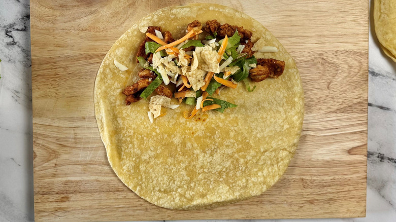 Tortilla on wooden board partially covered with chicken, lettuce, cheese, and tortilla chips