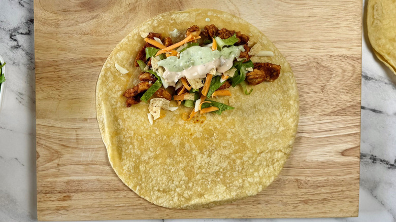 Tortilla partially covered with chicken, lettuce, cheese, and sauces
