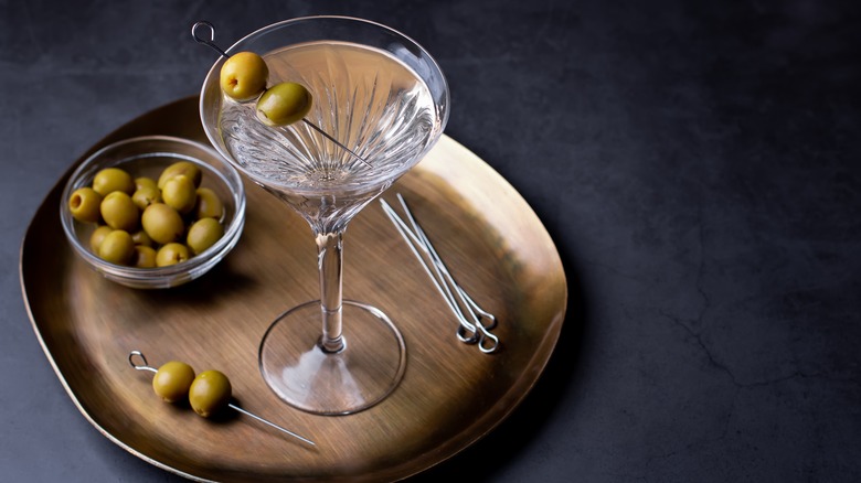 Dirty martini on gold serving platter with ramekin of olives