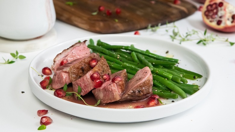 plate with sliced duck and green beans with pomegranate