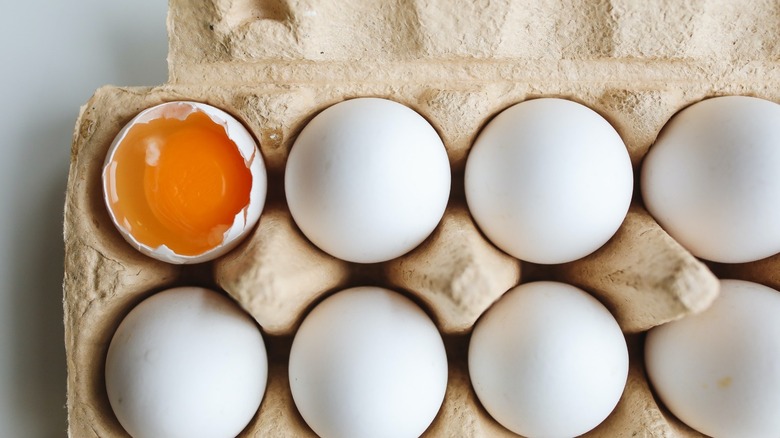 Eggs in a carton. One's cracked open.