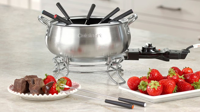 A Cuisinart electric fondue set on a countertop with pieces of chocolate and strawberries below.