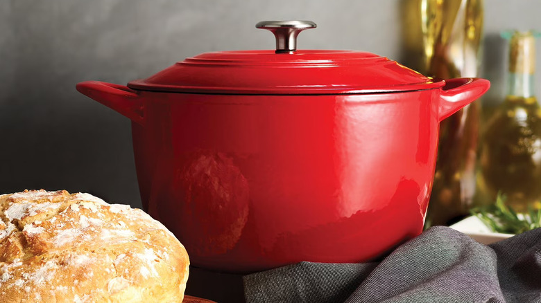 Red cast iron Dutch oven and a rustic loaf of bread.