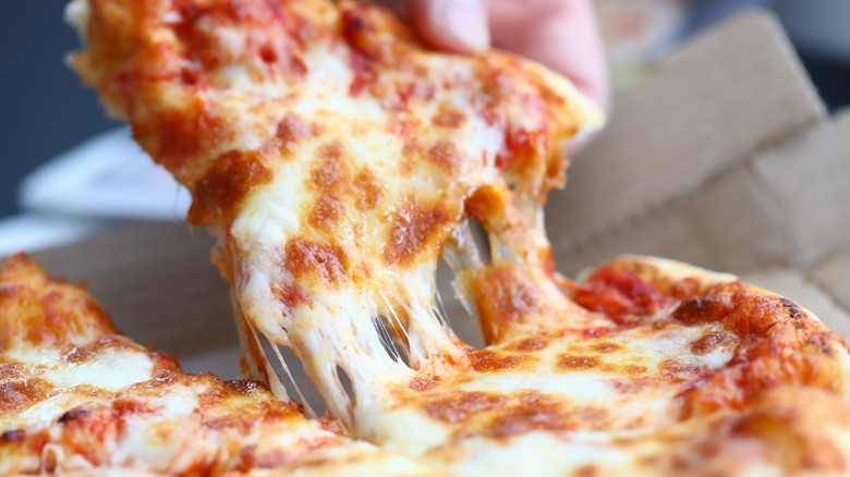 closeup of someone taking a slice of cheese pizza