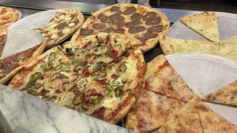 a row of pizzas and slices on metal trays at Secret Pizza in Las Vegas