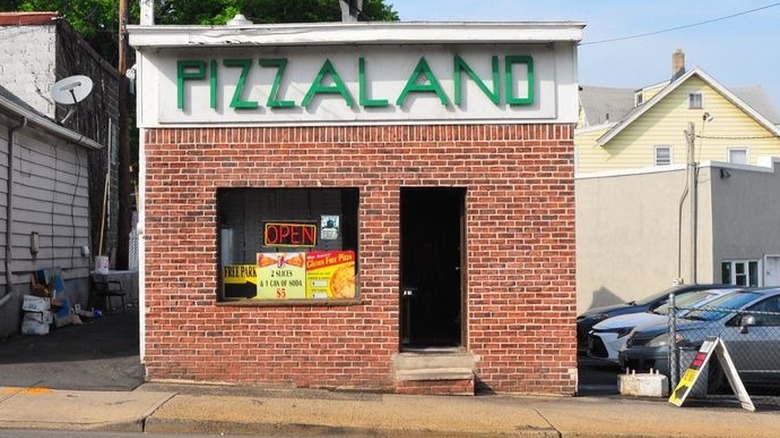 the iconic exterior of Pizza Land, a narrow brick building with neon open sign and Pizza Land sign above door