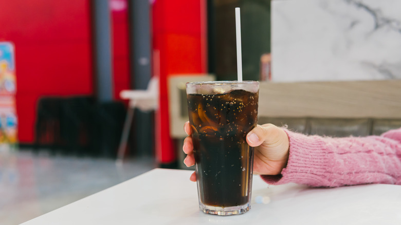 Someone sitting at a table holding a glass of coke with a white straw sticking out of it