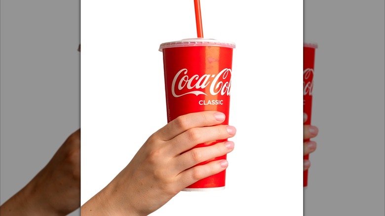 A hand holding up a Coke cup with a red straw and a plastic lid