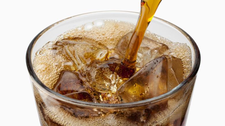 Cola being poured into a glass over ice on a white background