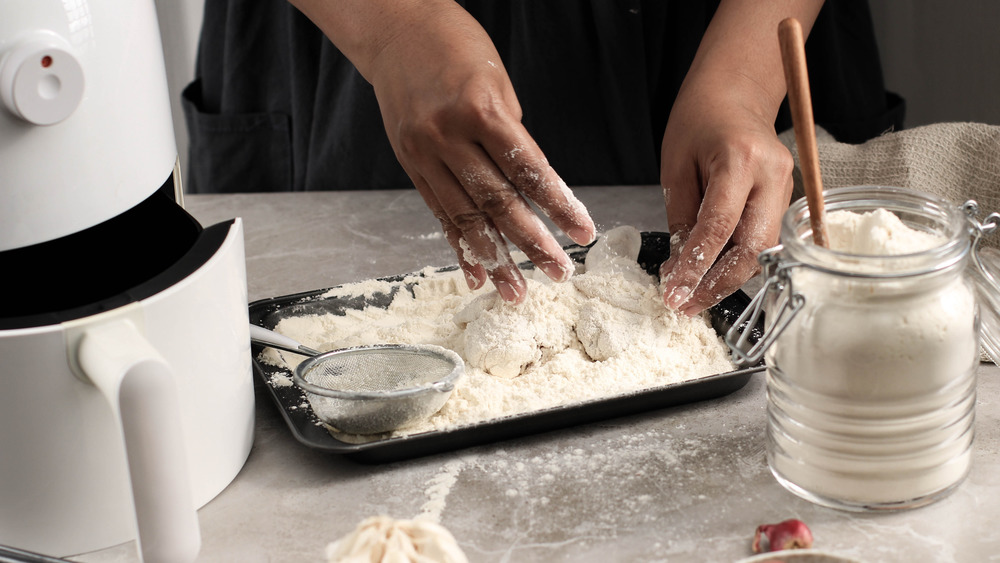 Person breading a piece of chicken with flour