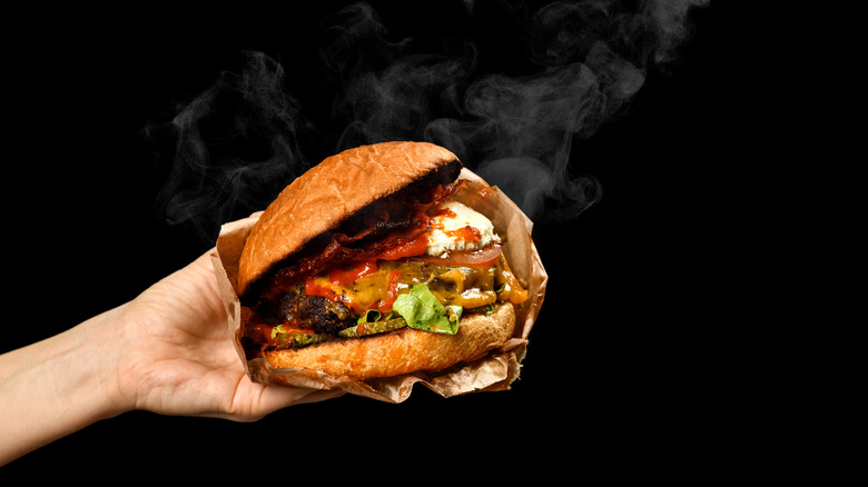 A person holding a messy cheeseburger