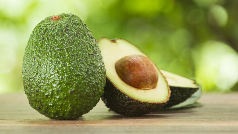 Whole and cut avocados on wooden board