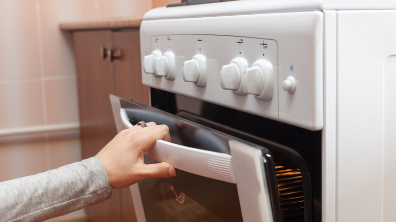   Mano che apre la porta di un forno bianco