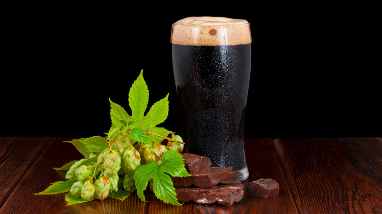 Glass of dark stout beer with hops and chocolate by it